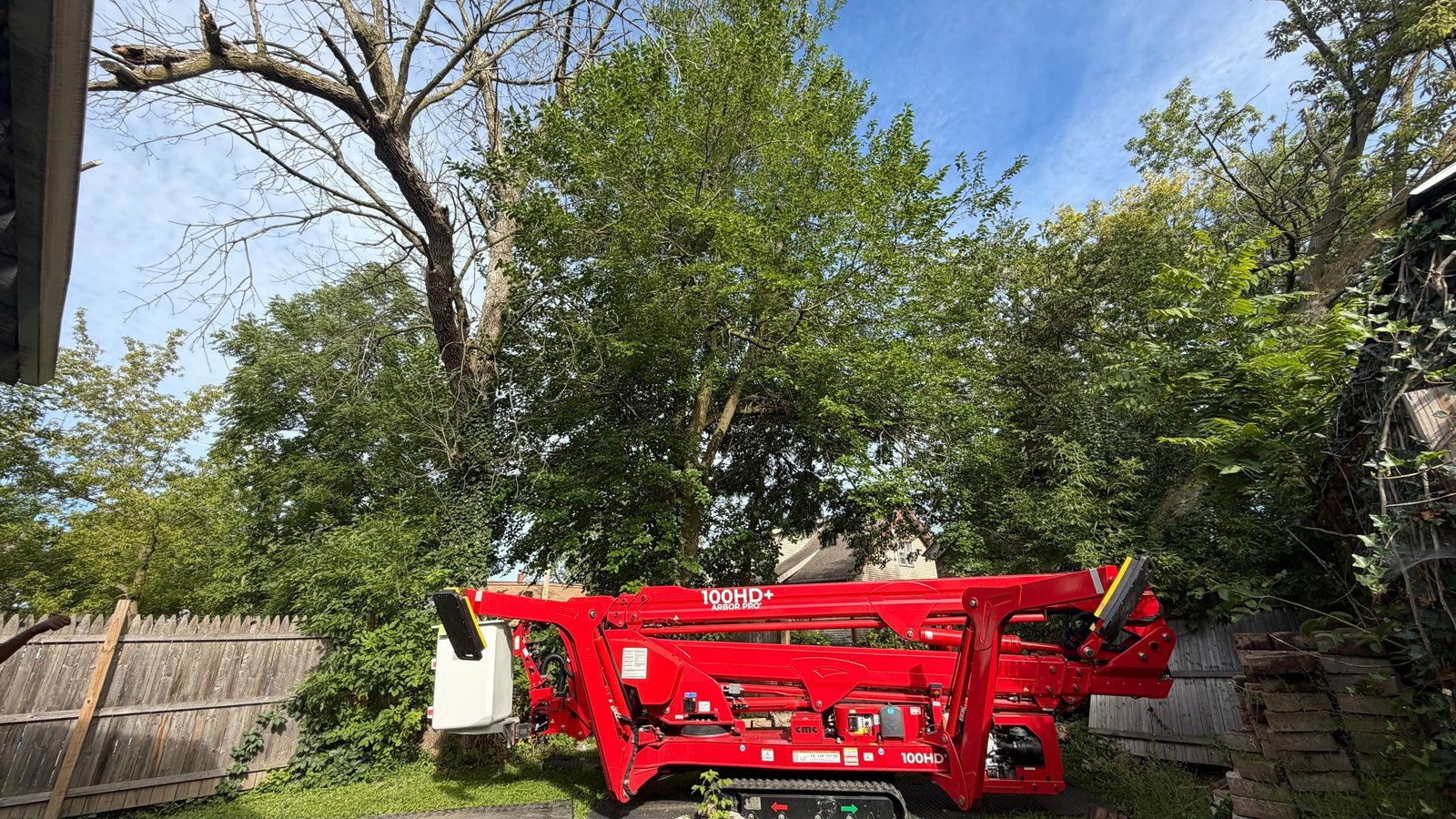 Folded red spider lift positioned beneath trees in a backyard